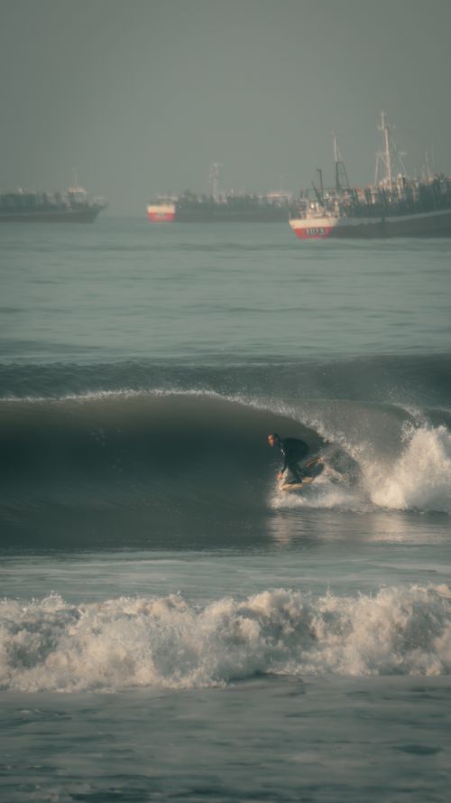 Free A surfer skillfully rides a wave with ships in the background at Mar del Plata, Argentina. Stock Photo