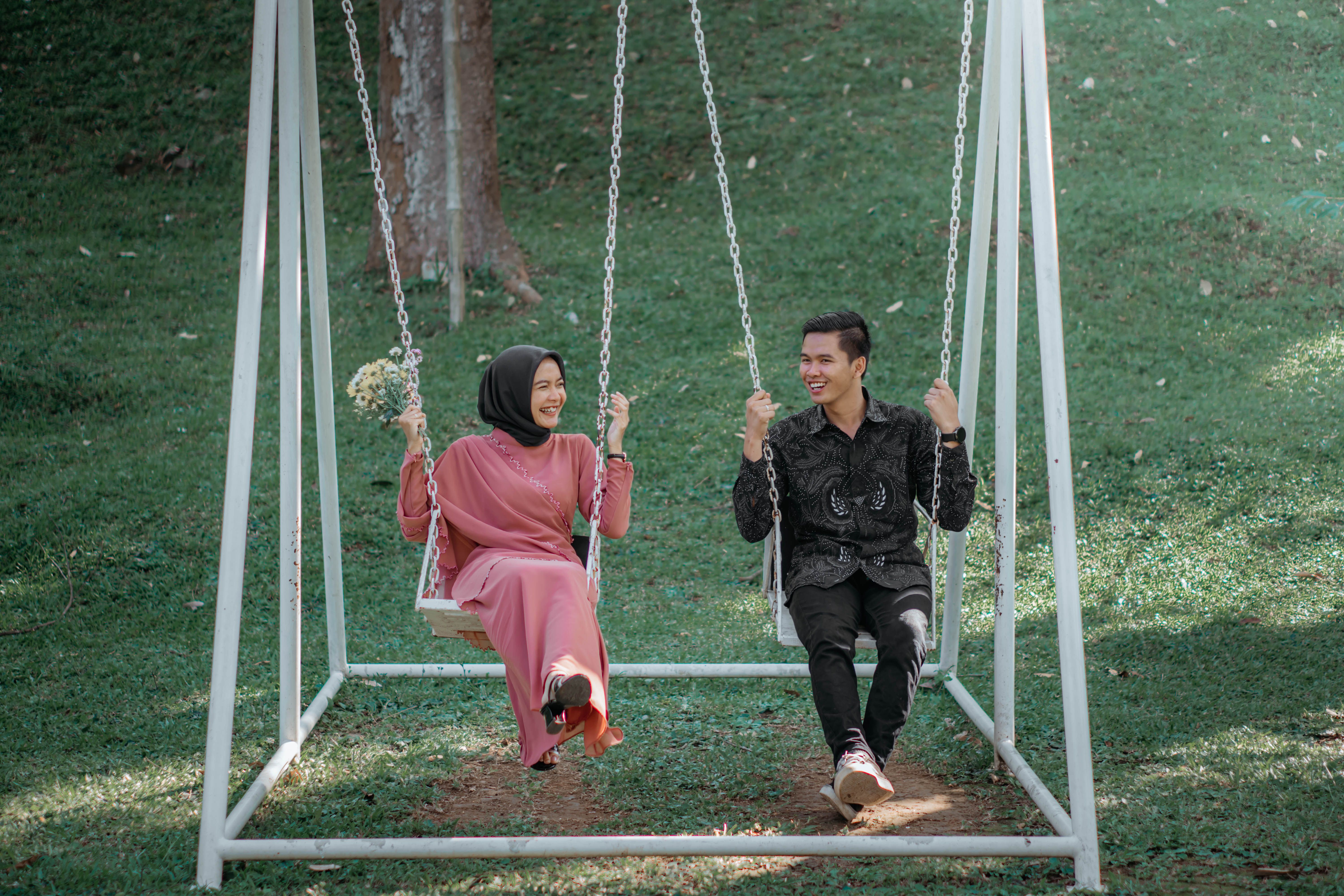 A happy couple sitting on a swing in a park, enjoying a sunny day together.