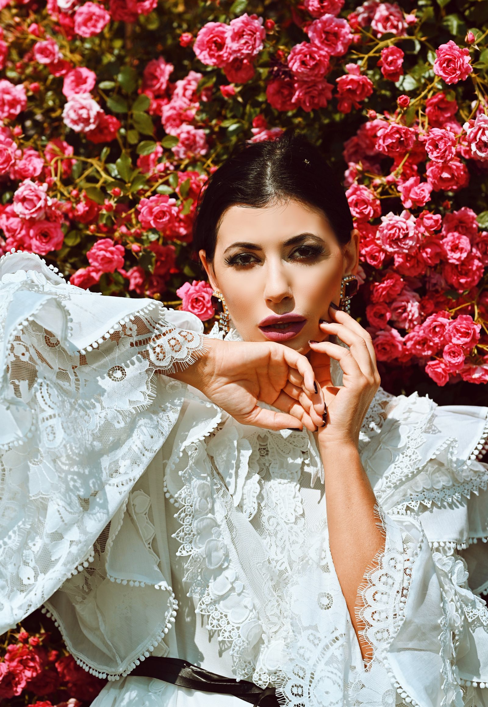 An elegant woman in a voluminous white lace ruffled dress amid roses — the return of the ruffle for summer 2026