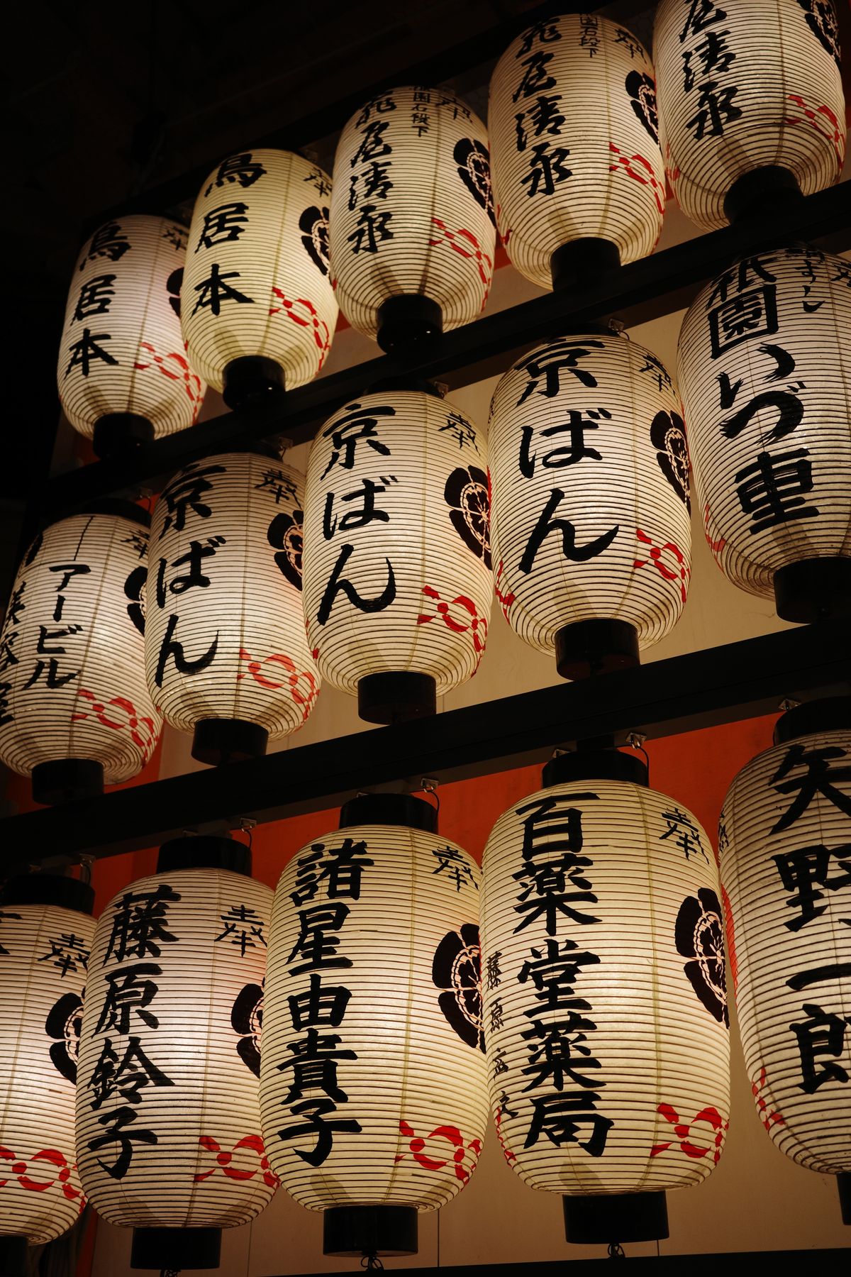 Paper lanterns painted with kanji characters illuminated during a nighttime Japanese festival, similar to the glowing nebuta floats of Aomori