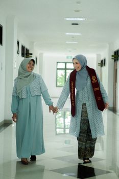 Two women in hijabs celebrate graduation with smiles and traditional attire. - Fotografer Sidoarjo