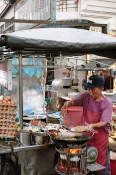 A street food vendor cooks Asian cuisine in a bustling outdoor market.