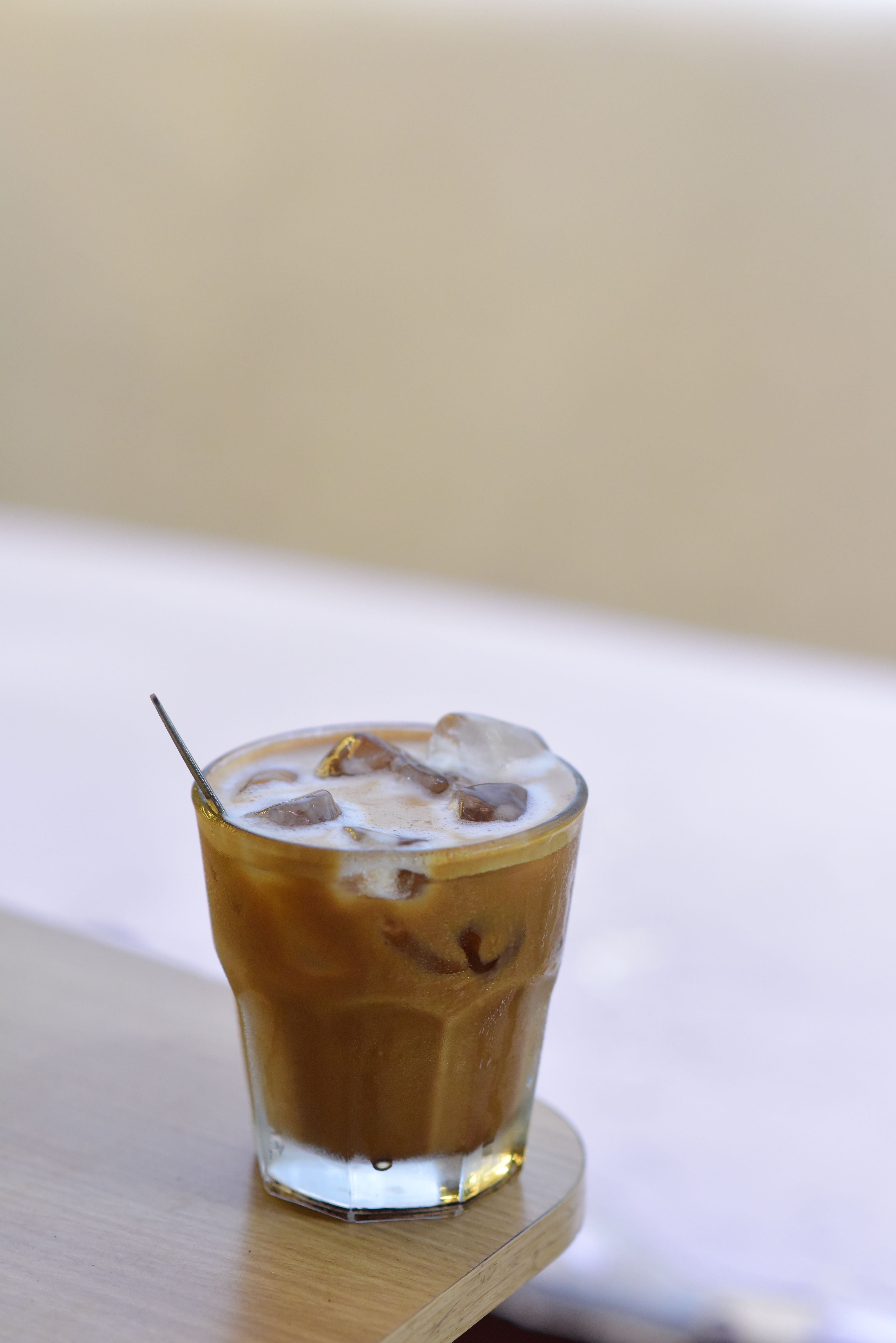 Delicious iced coffee in a glass with milk foam and ice cubes on a wooden table.