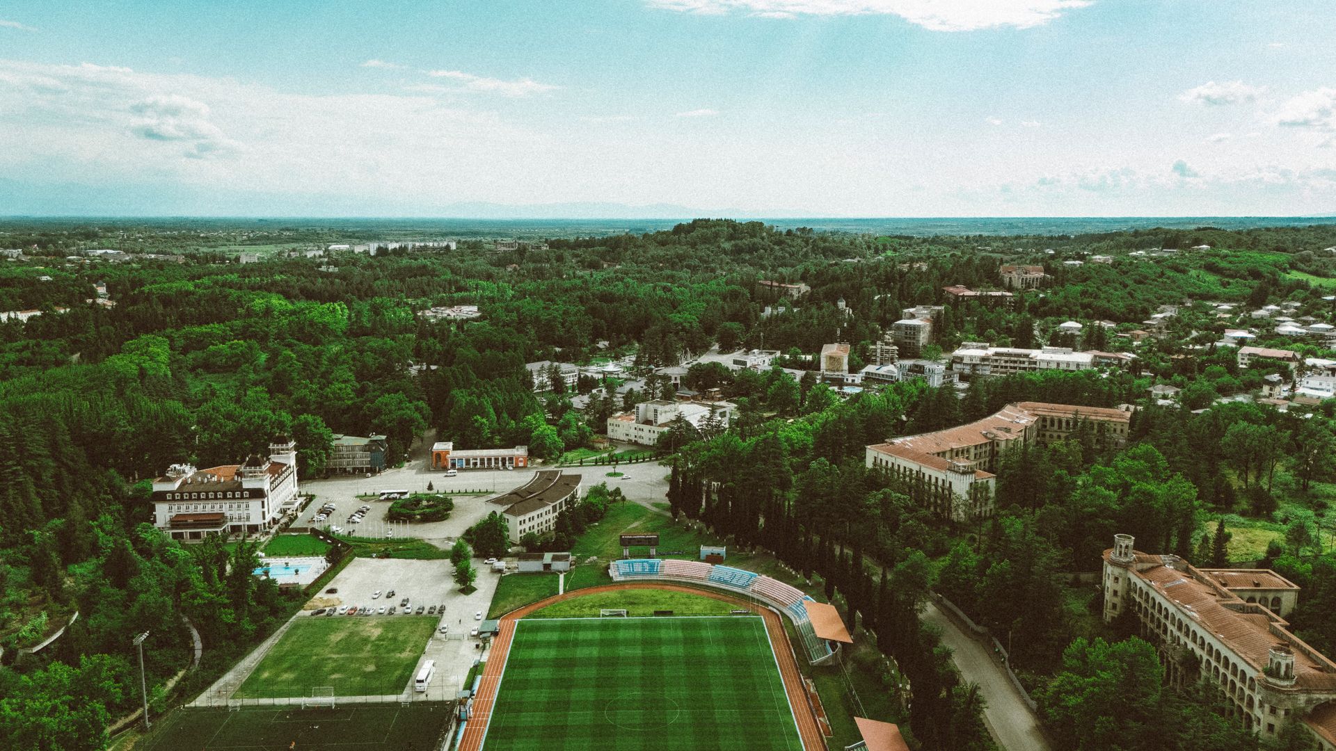 Aerial view of lush greenery and urban landscape in Georgia with a visible sports field and buildings.