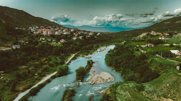 A stunning aerial shot of Georgia's greenery and river winding through hills under a dramatic sky.