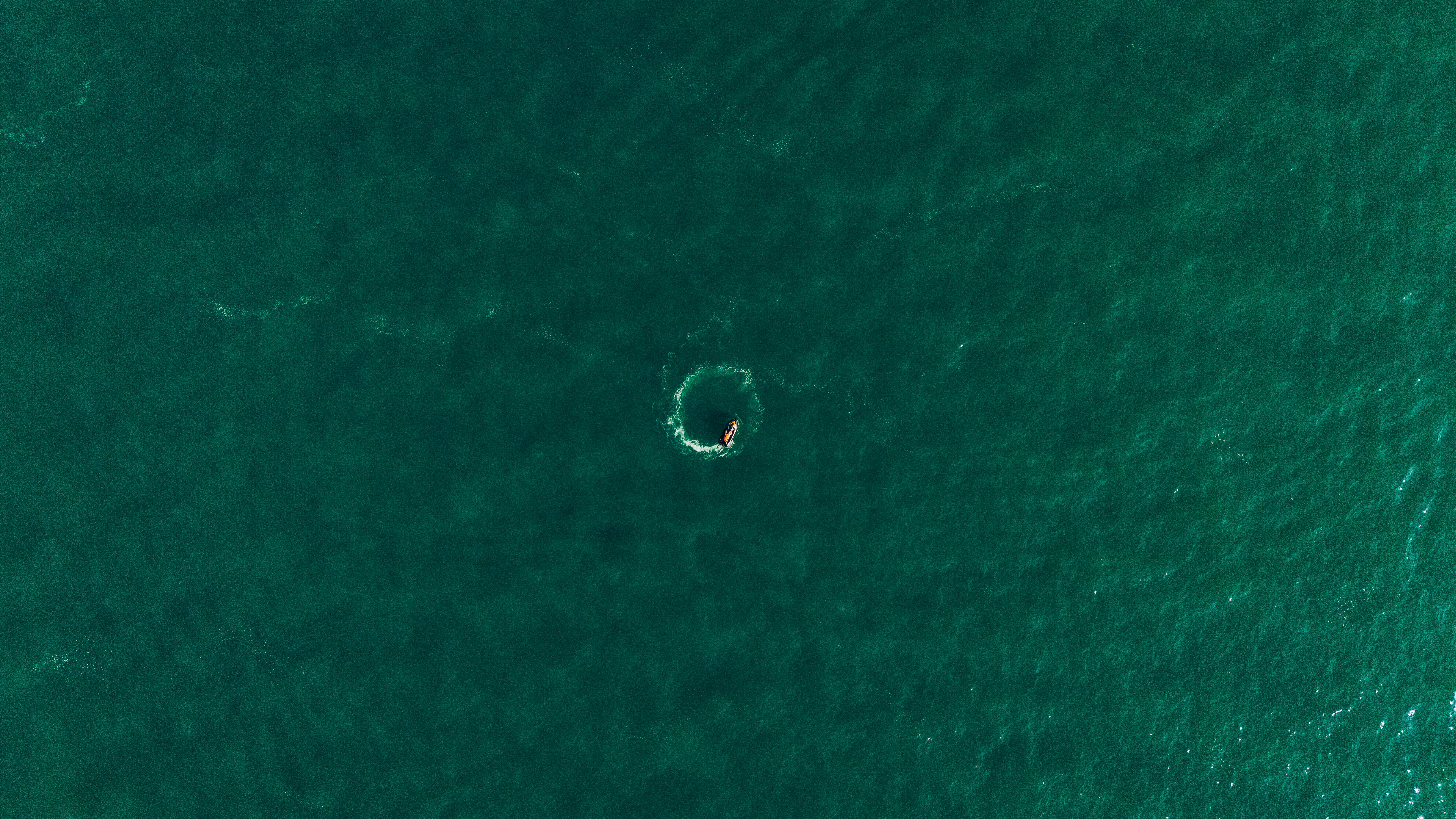 Un dron captura a un kayakista solo rodeado por vastas aguas verdes del océano.