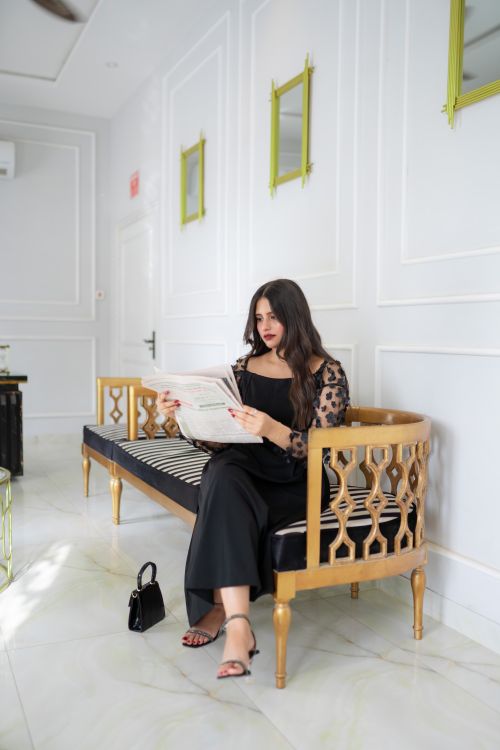 Free Woman sitting on stylish bench reading a newspaper in a bright, elegant room. Stock Photo