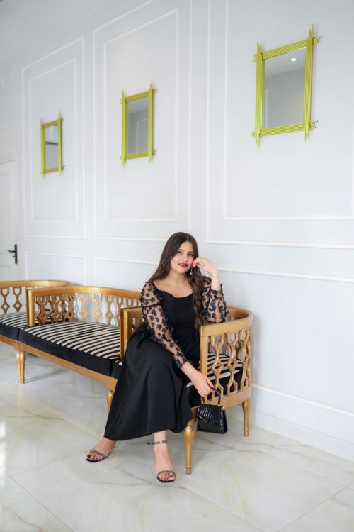 Free Woman in a stylish black outfit sitting in a modern, elegant white room with artistic decor. Stock Photo