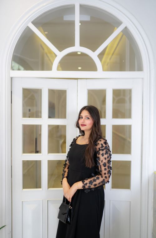 Free Portrait of a woman in a stylish black dress standing by a white arched doorway indoors. Stock Photo