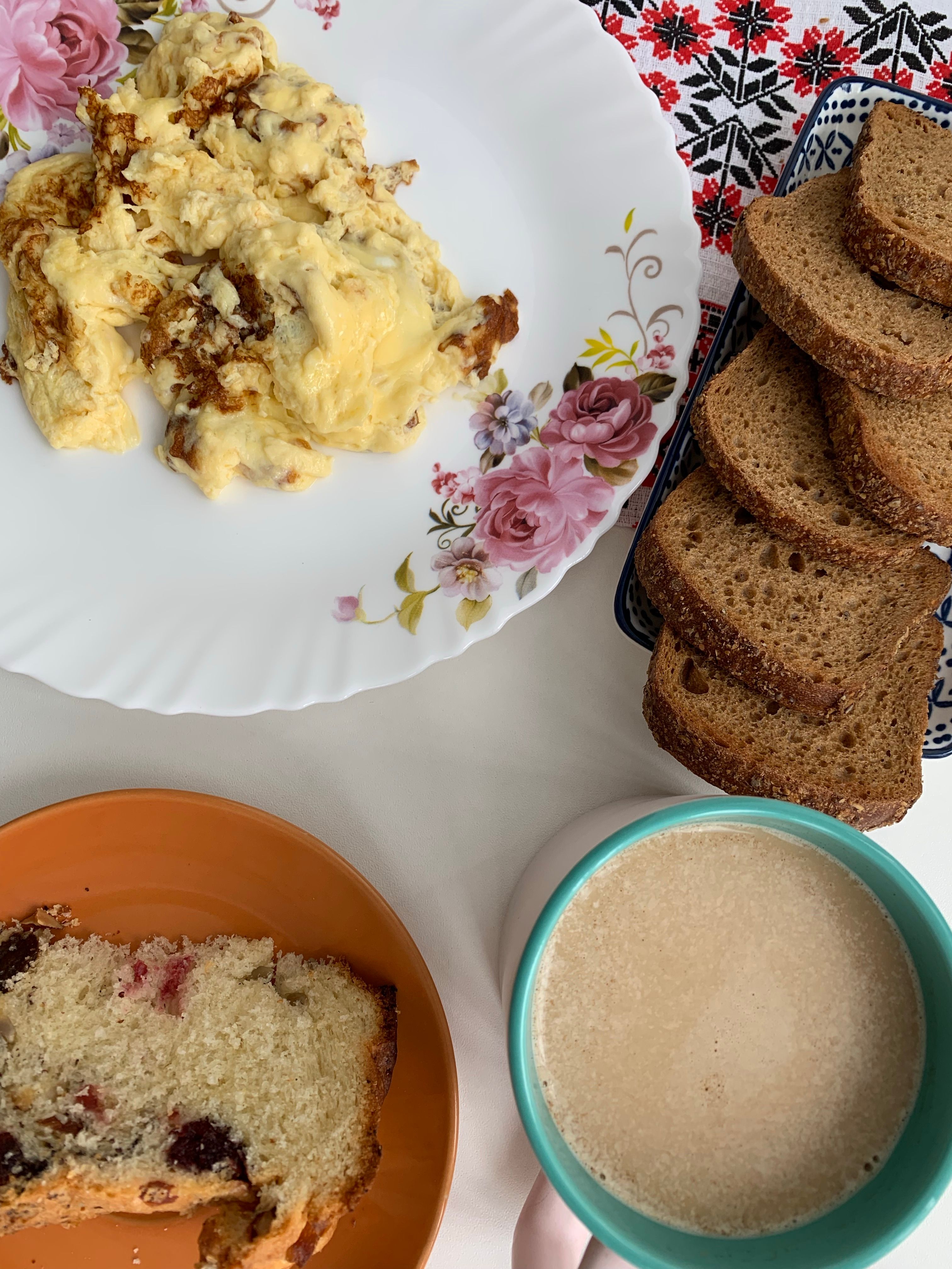 A delicious breakfast spread featuring scrambled eggs, bread slices, fruitcake, and a cup of coffee.