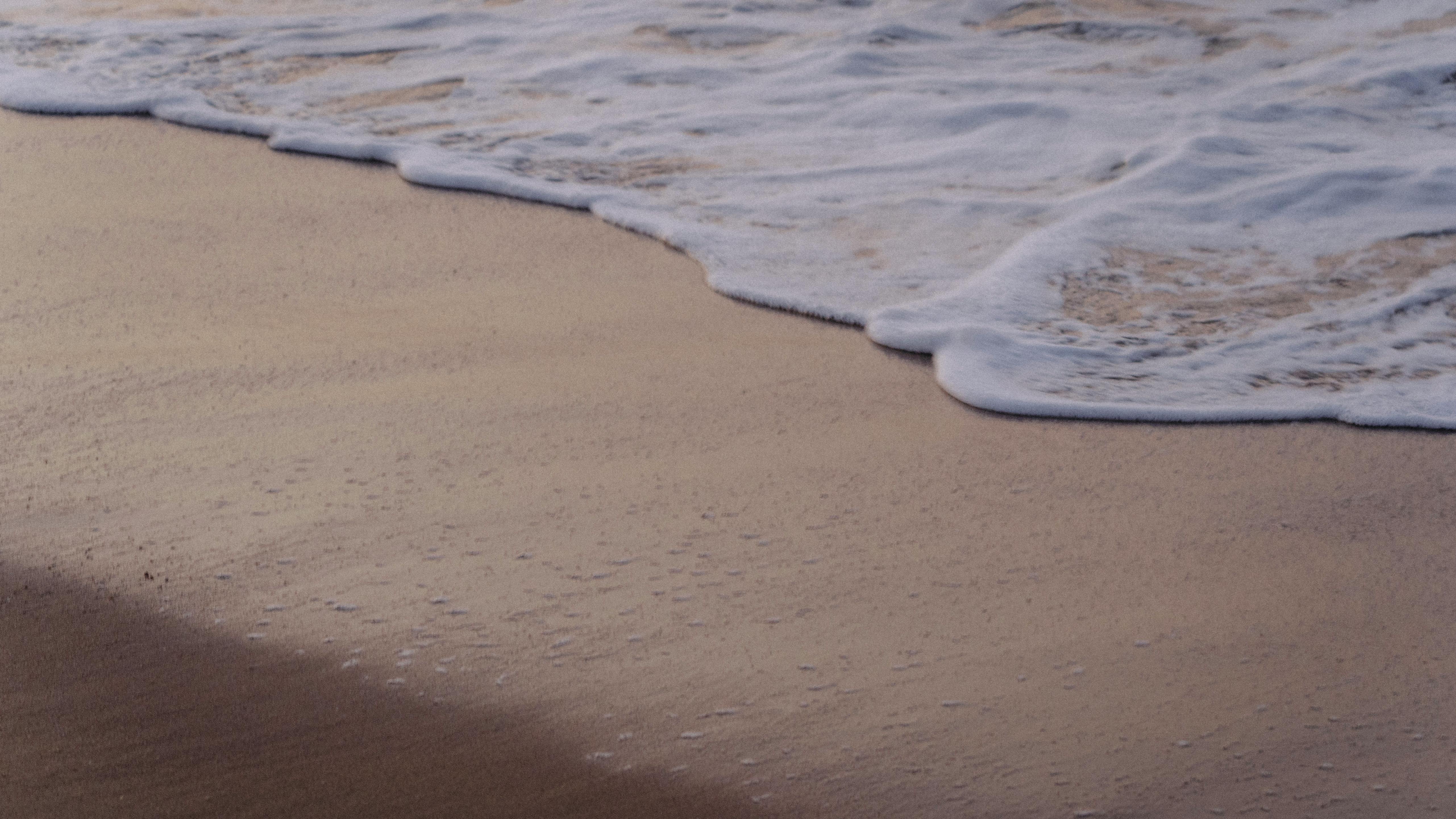 Gratis Le onde morbide lambiscono dolcemente la riva sabbiosa nella calda luce del tramonto, creando uno scenario di pace. Foto a disposizione
