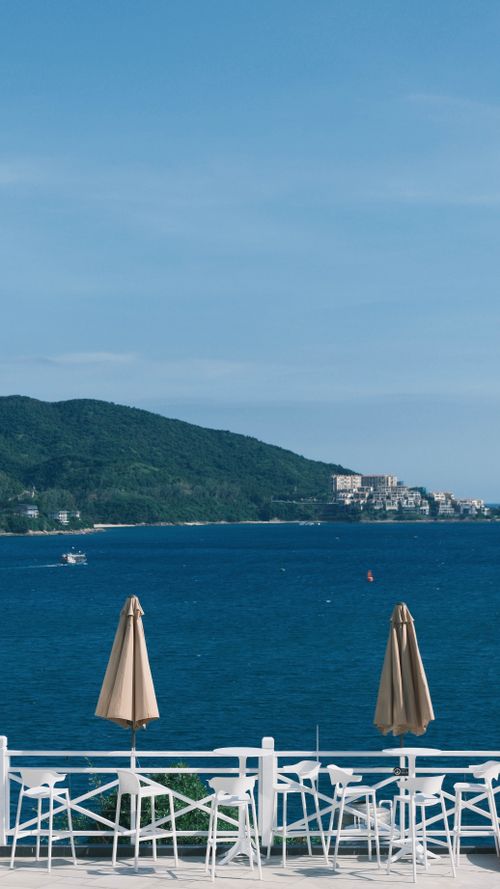 Free Tranquil seaside scene with umbrellas, clear blue sea, and distant landscape. Stock Photo