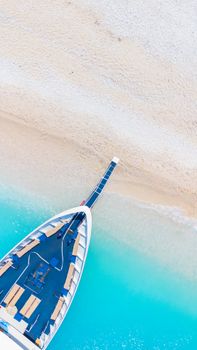 Stunning aerial shot of a sailboat docked on a pristine sandy beach with turquoise water.