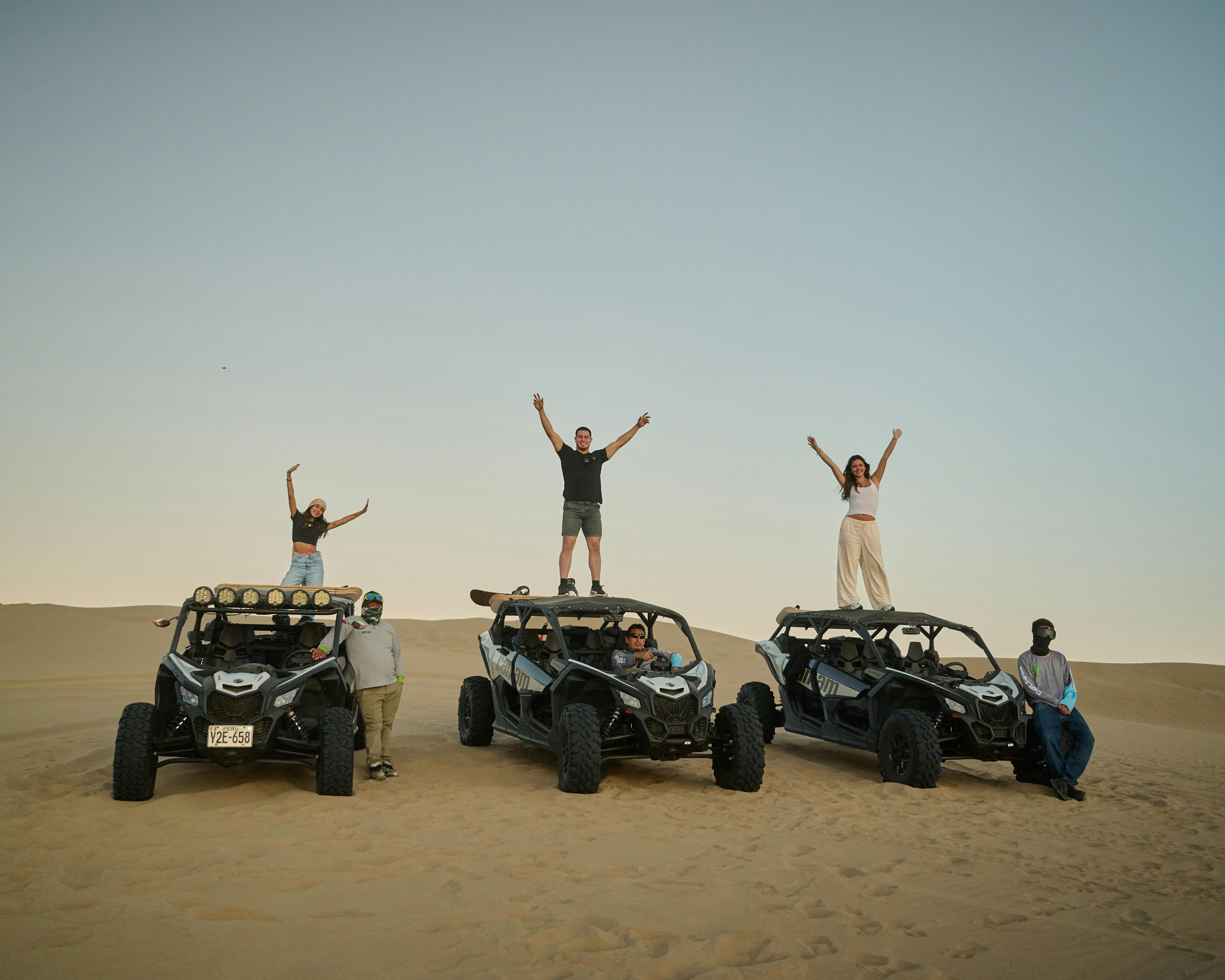 Enthusiastic group enjoying a desert adventure with dune buggies at sunset.