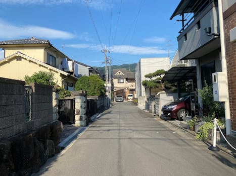 View of a calm residential street in Ashiya, Japan, with houses and parked cars under a blue sky.
