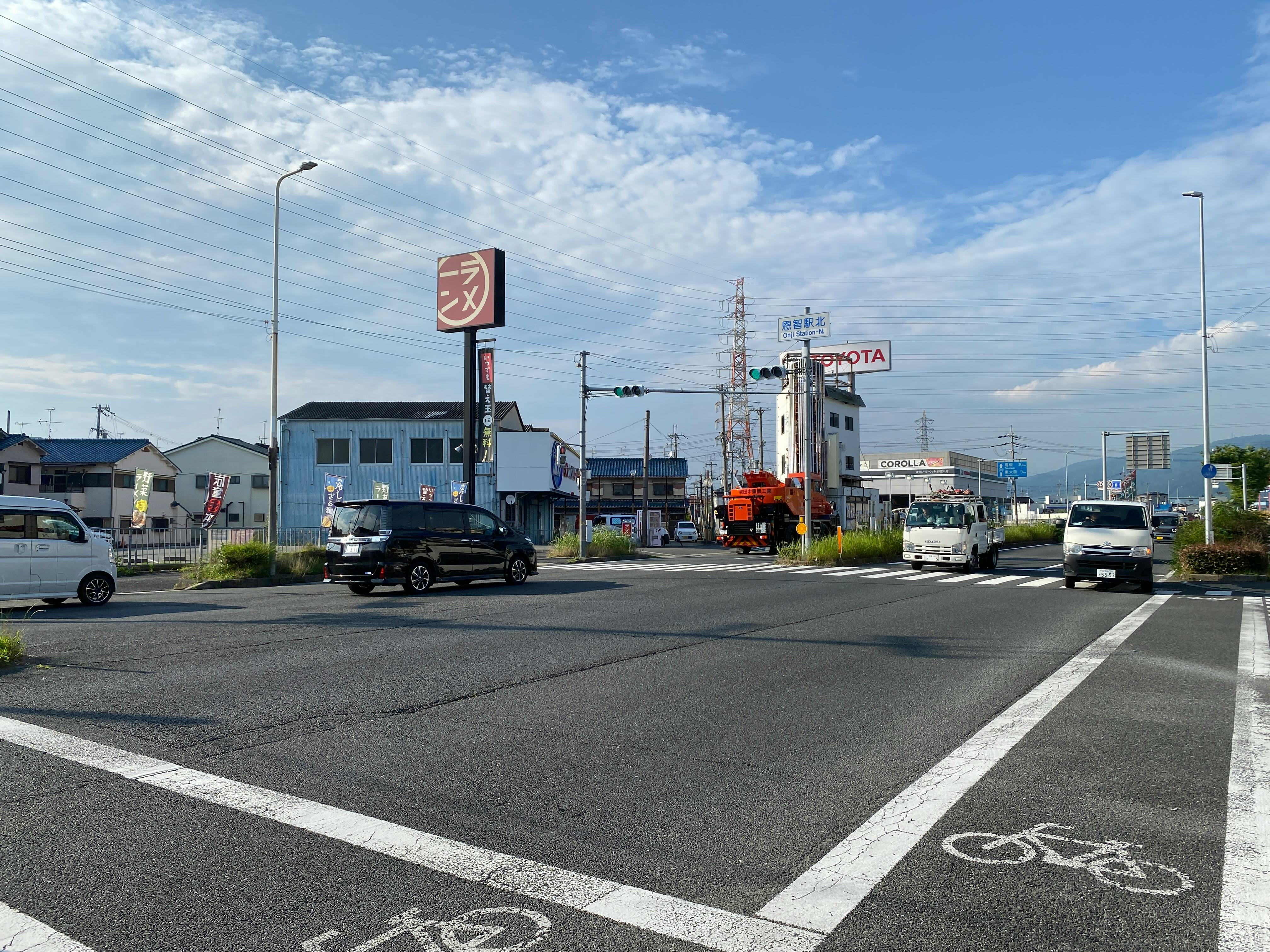 Street intersection in Amagasaki, Japan with cars and signage under a blue sky.