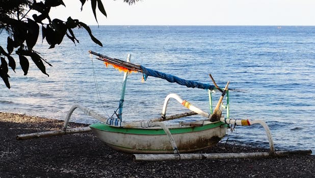 A traditional fishing boat rests on a pebble beach in Amed, Bali, overlooking the calm ocean waters.