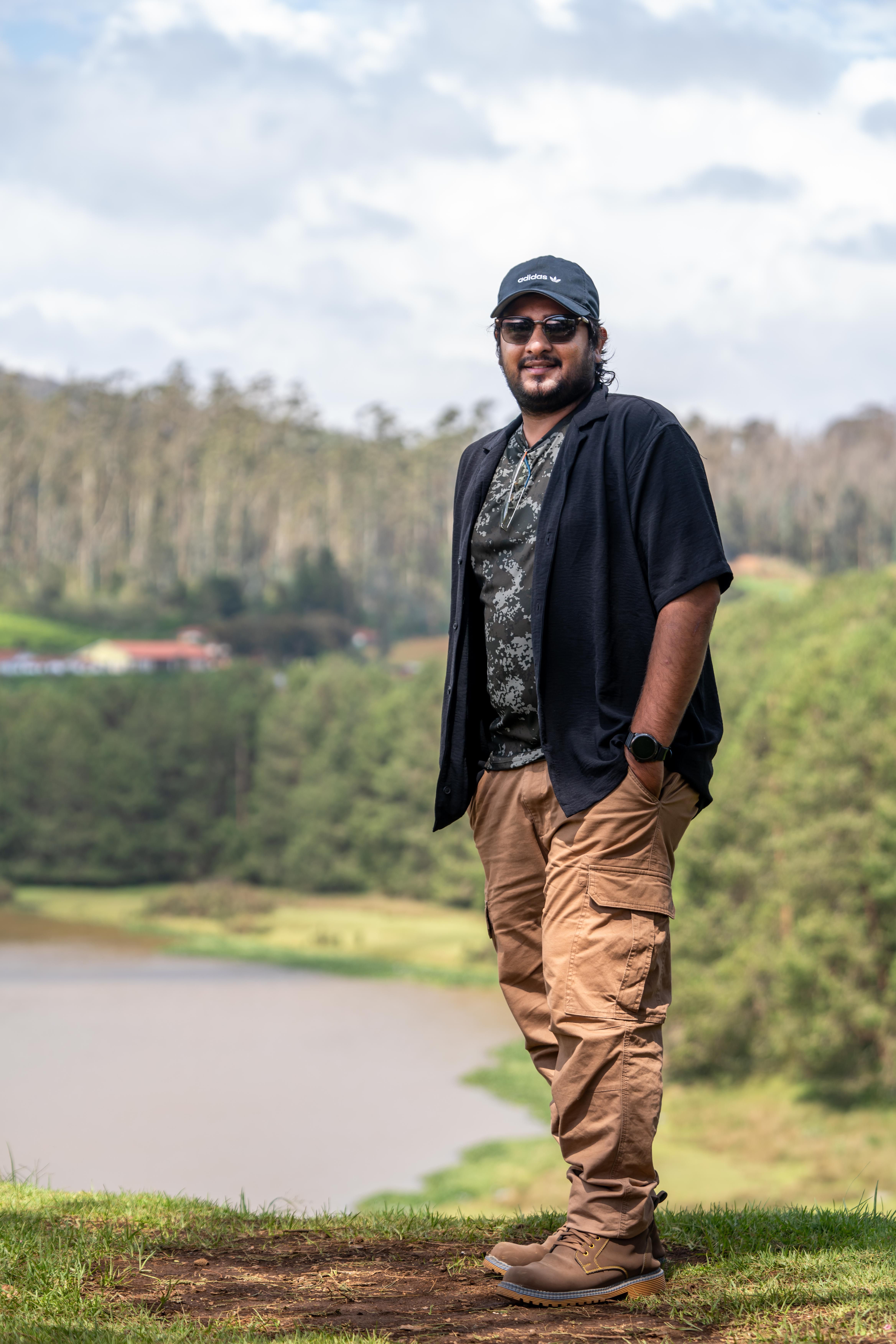 Young man posing casually in a natural forest setting by a scenic lake.