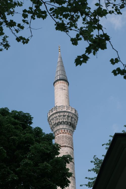 Free A beautiful Ottoman-style minaret framed by trees, set against a clear blue sky in Istanbul, Türkiye. Stock Photo