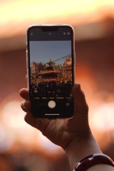 A person captures vibrant Bhaktapur festival scene using a smartphone camera outdoors.