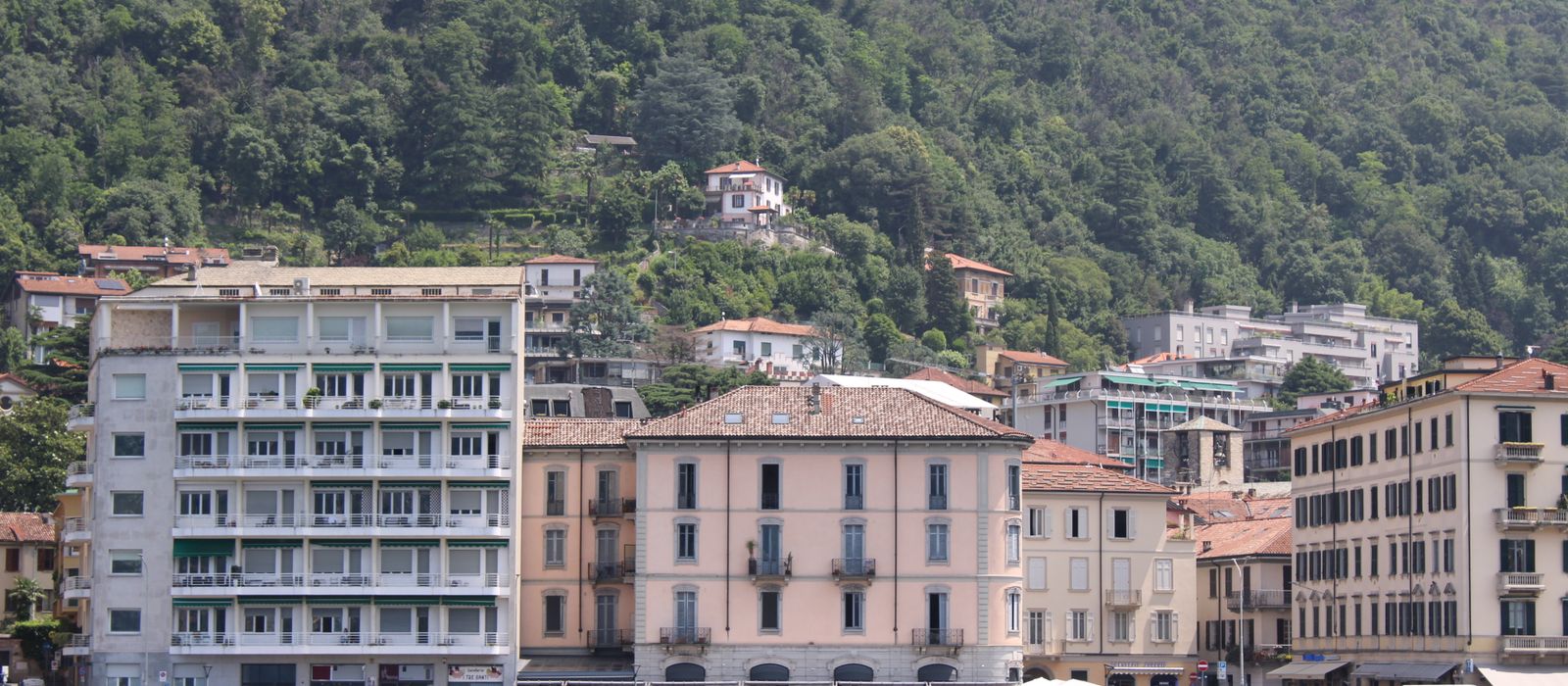 A picturesque view of Lake Como's lakeside architecture with lush green hills in the background.