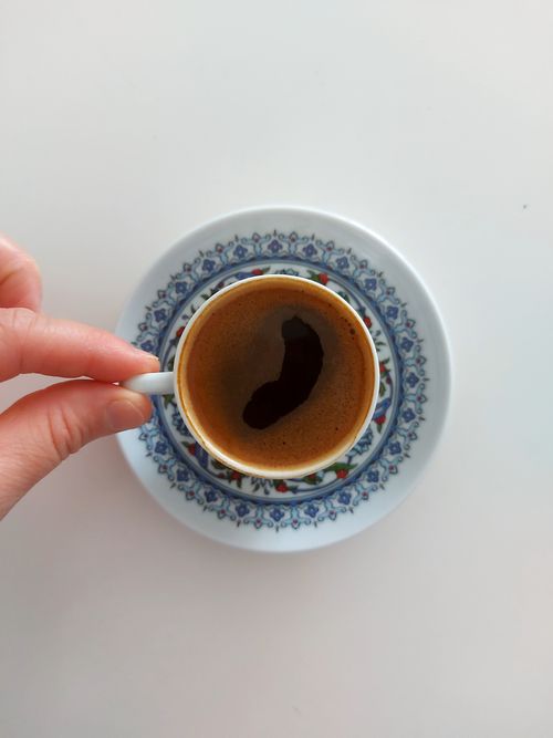 Free Top view of a hand holding a decorative Turkish coffee cup on a patterned saucer. Stock Photo