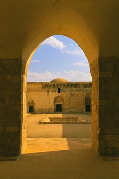 Explore the serene beauty of an ancient courtyard through a stone archway, under a vibrant blue sky.