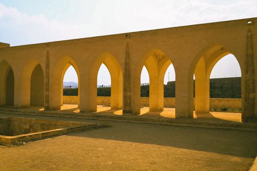 A row of ancient stone arches casting shadows under a bright sky, showcasing historical architecture.