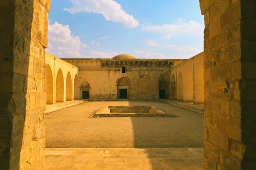 Historic stone courtyard with arches, warm tones, and blue sky.