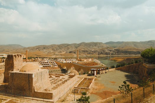 Explore the ancient ruins set against a backdrop of mountains and a winding river under a bright sky.