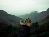 一只手握着一片小绿叶，在朦胧的山间背景映衬下，象征着大自然的宁静