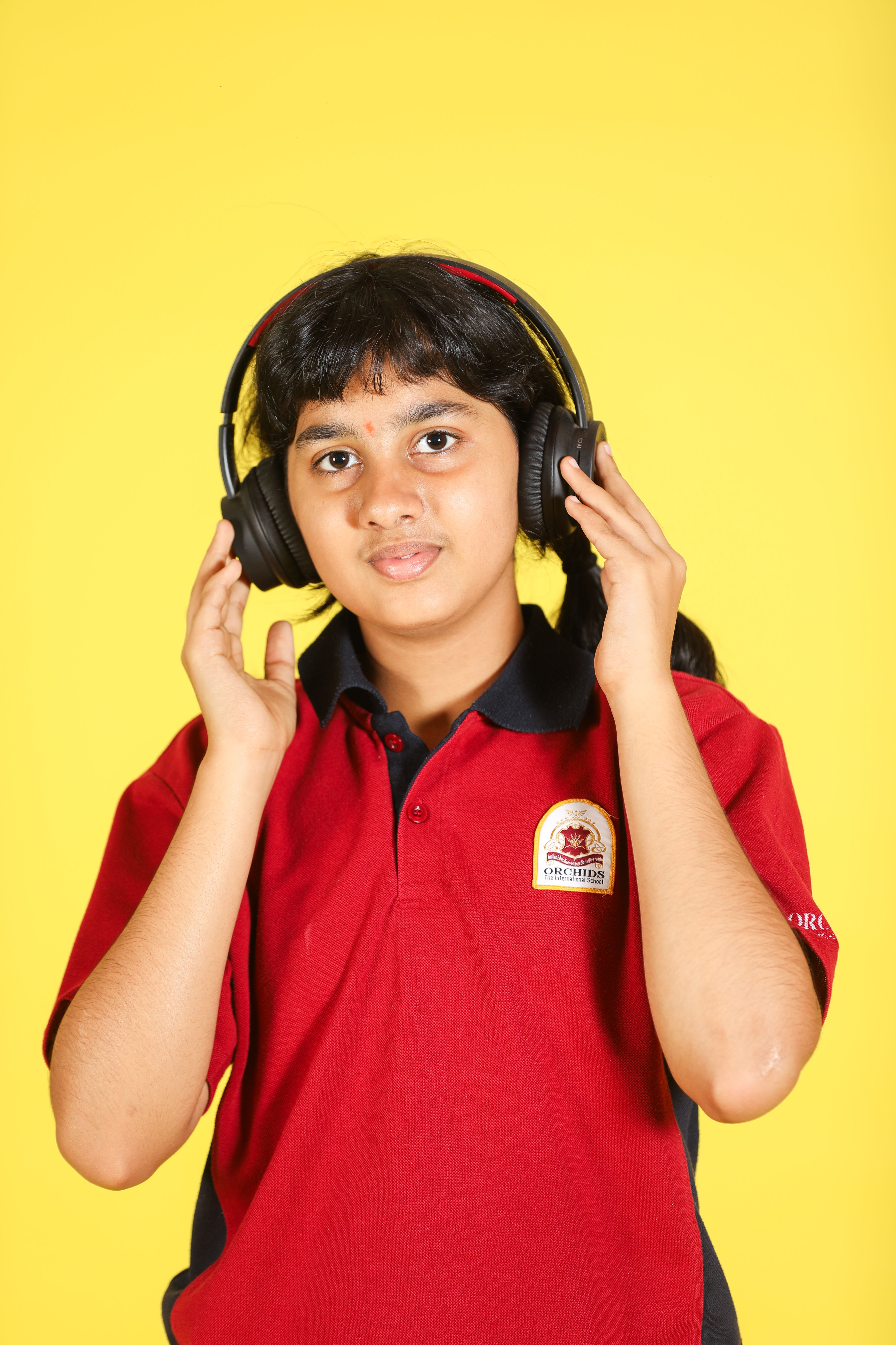 Teenage girl enjoying music with headphones against a vibrant yellow backdrop.