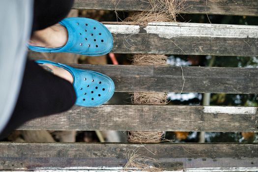 Person wearing blue sandals standing on wooden slats with water below, creating a rustic outdoor feel.