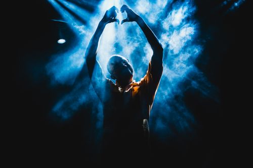 Free A person forms a heart with hands in dramatic stage lighting and smoke. Stock Photo