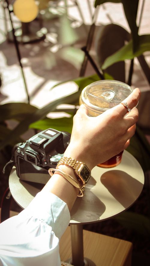 Free Hand holding iced coffee near a camera on a sunny afternoon. Modern lifestyle. Stock Photo