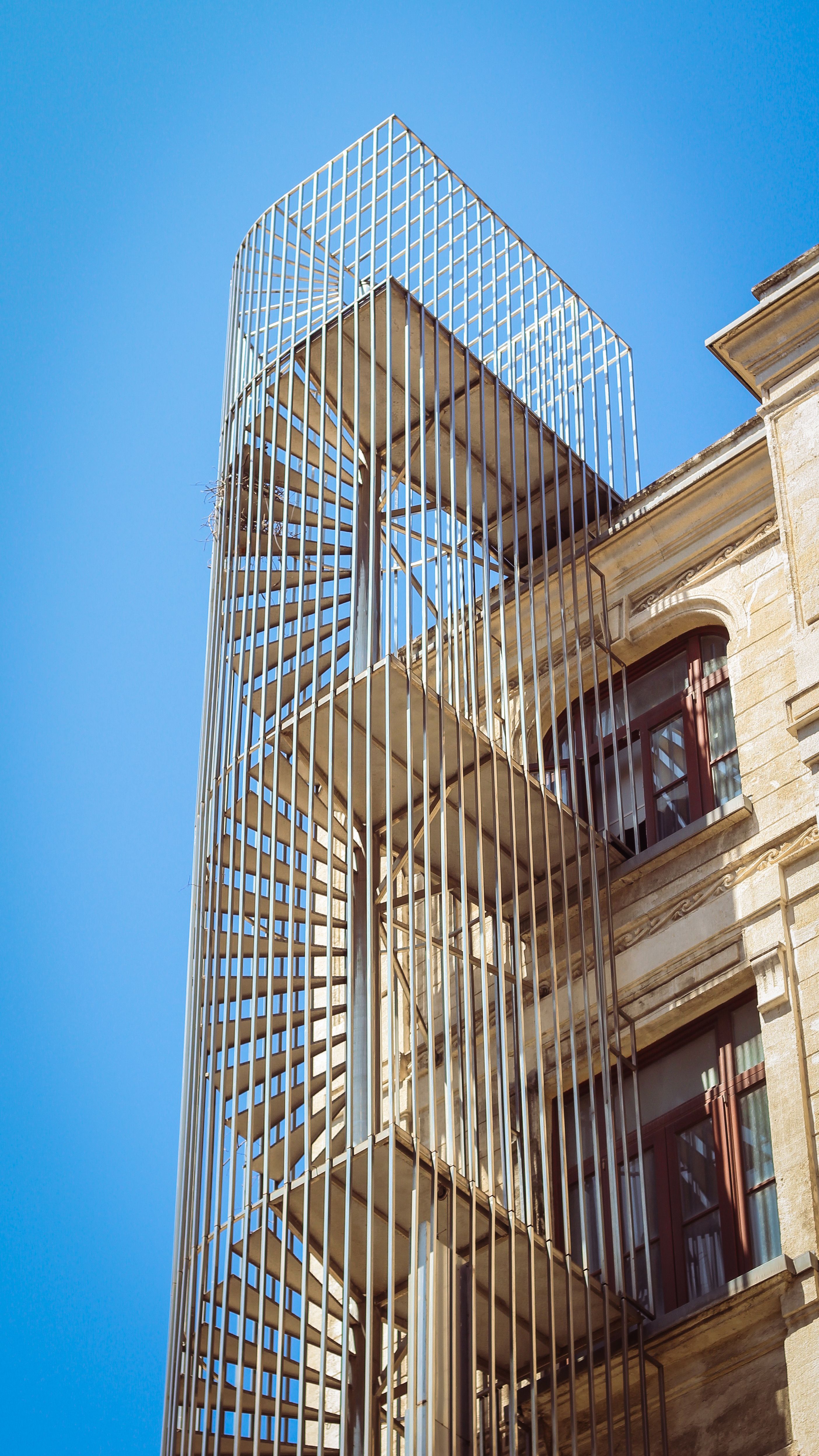 Escalier hélicoïdal métallique protégé par une cage, contre une façade en pierre