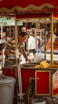 Street vendor preparing fresh grilled corn at a busy outdoor market, bustling with shoppers and vibrant colors.