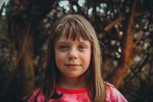 Free A young girl with bangs smiles gently in an outdoor park setting. Stock Photo