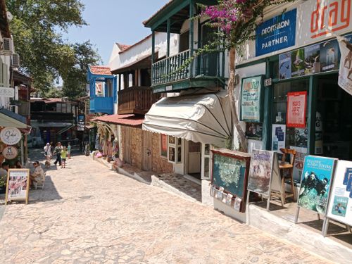 Free Explore a sunlit Mediterranean street lined with vibrant shops and visitors enjoying a leisurely stroll. Stock Photo