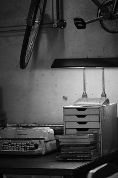 A vintage study room scene featuring a typewriter, stack of books, and a bicycle wheel.