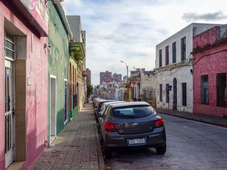 Street scene in Montevideo with colorful buildings and parked cars under a bright sky.