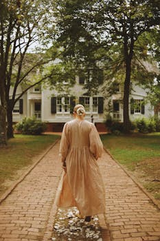 Woman in a flowing dress walks a brick path towards a historic house in NC.