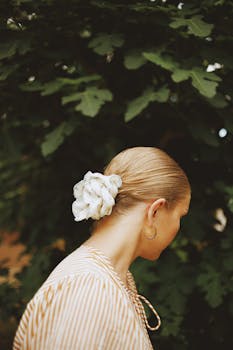 Elegant woman turned away, showcasing a flower hair accessory, amidst lush greenery.