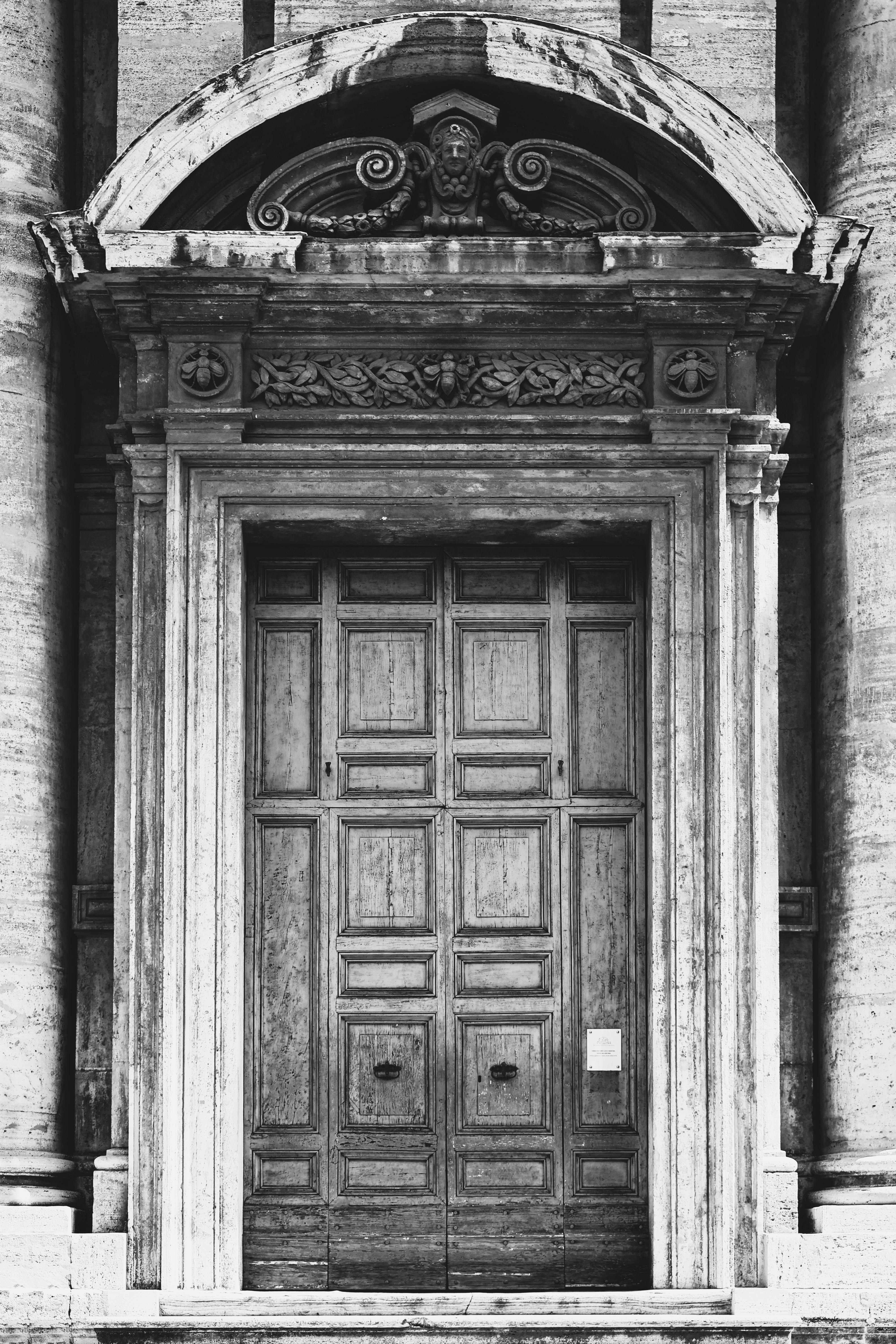 Bezpłatne Czarno-białe zdjęcie zdobionych drewnianych drzwi kościoła w Rzymie, ukazujące misterną architekturę. Zdjęcie z galerii