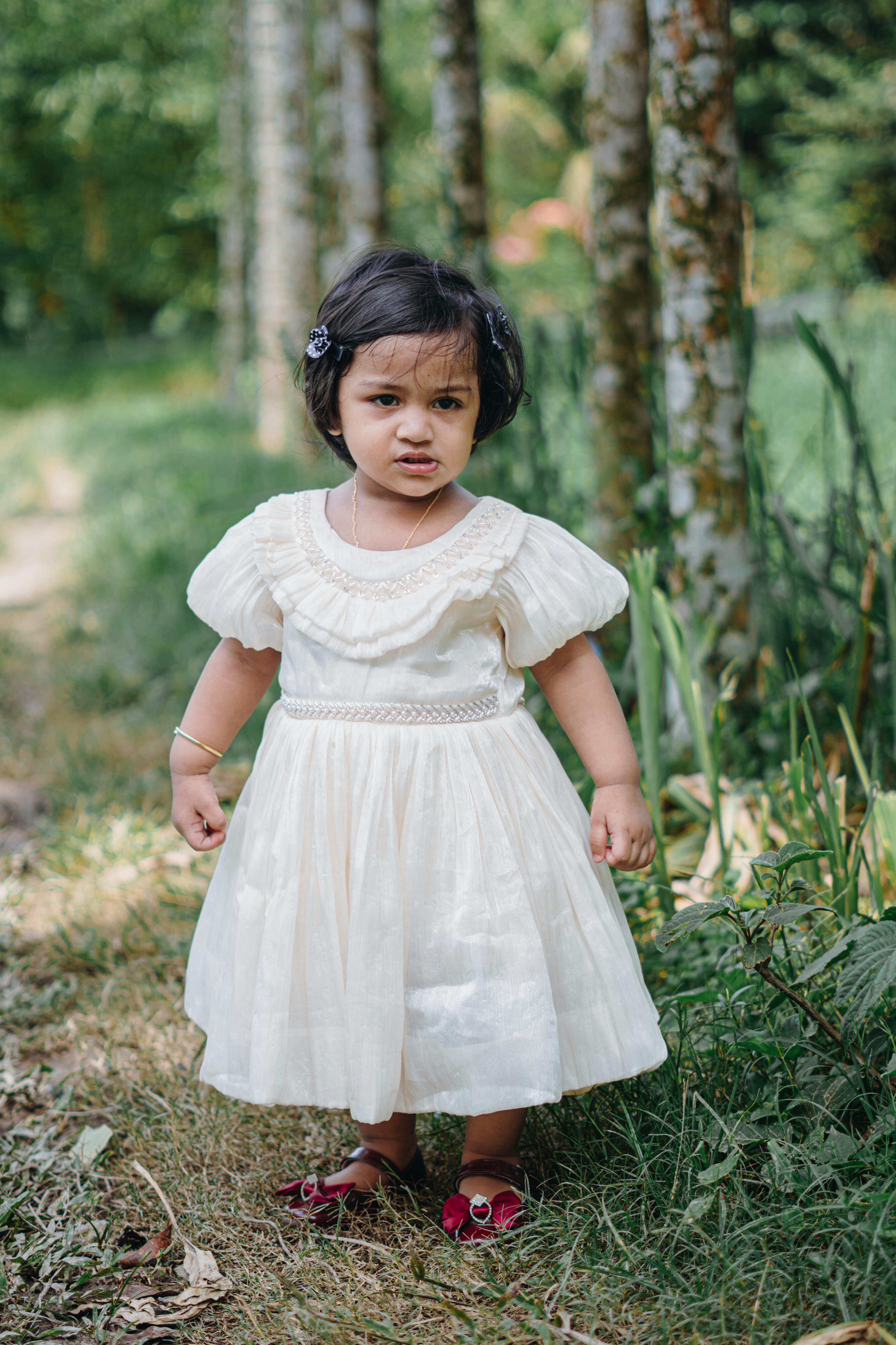 Gratis Adorabile ragazzina in abito bianco in piedi su un lussureggiante sentiero nella foresta Foto a disposizione
