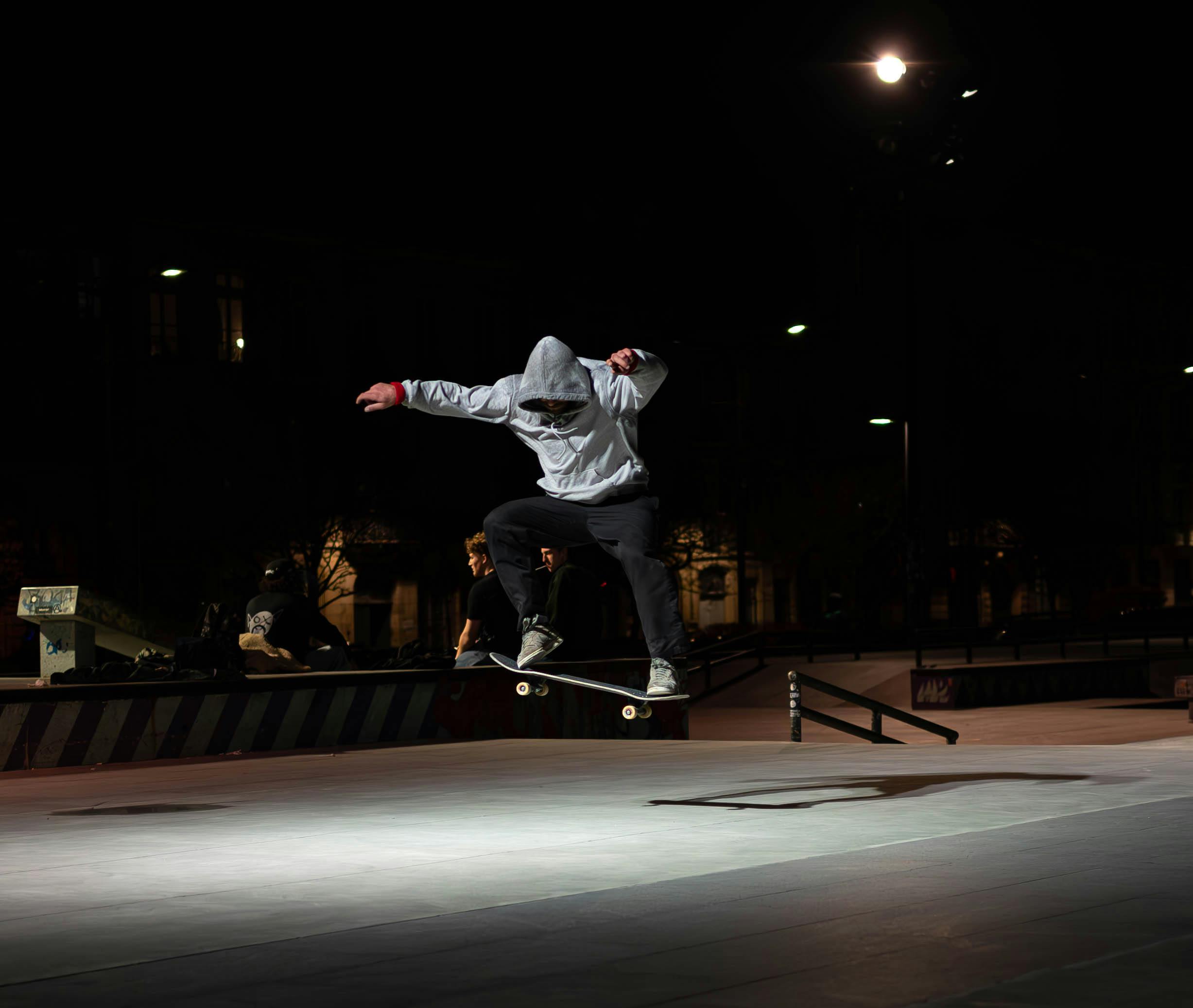 A skateboarder performs a trick in a well-lit urban skatepark at night in Bordeaux, France.