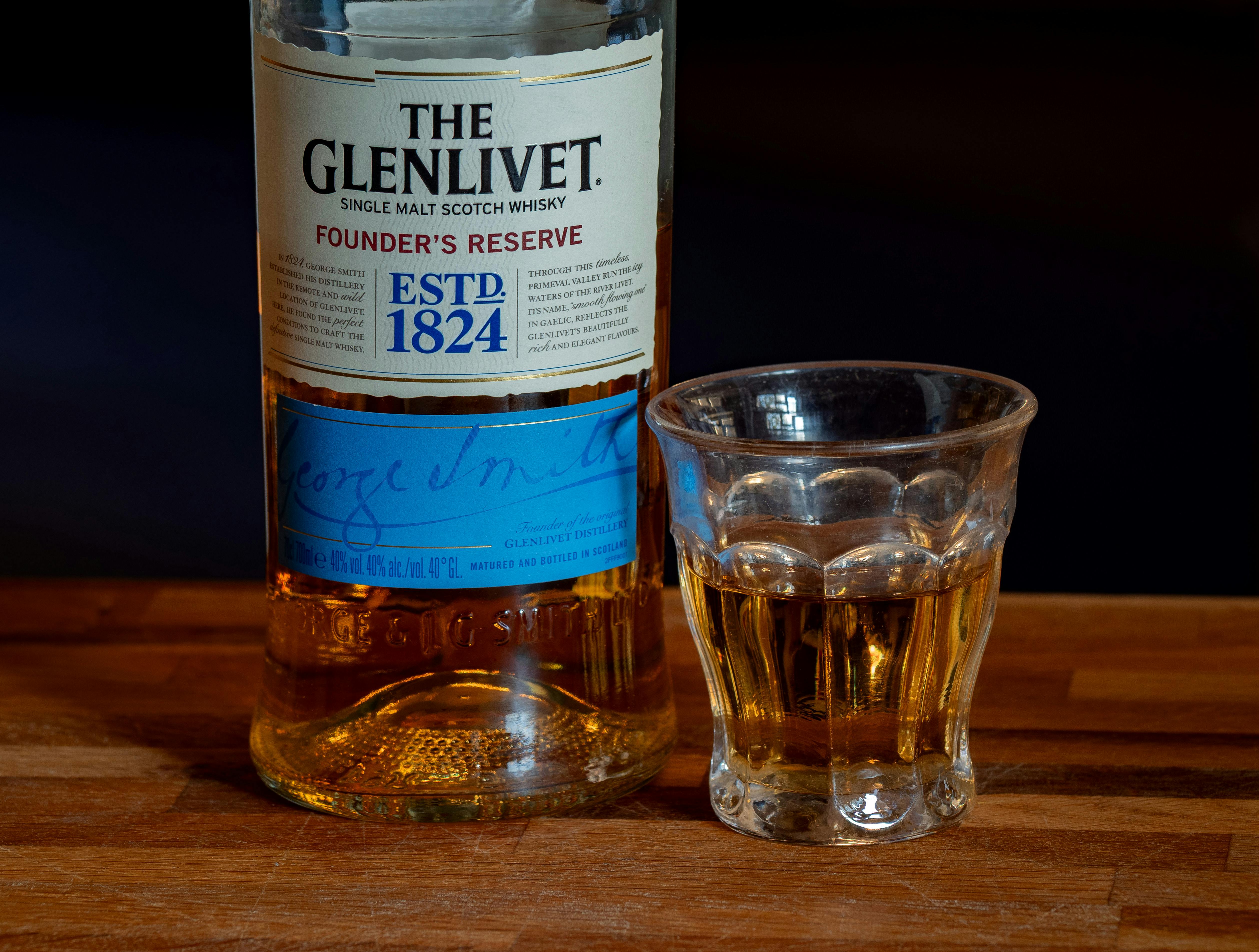 Close-up of The Glenlivet Founder’s Reserve whisky with a glass on a wooden surface.