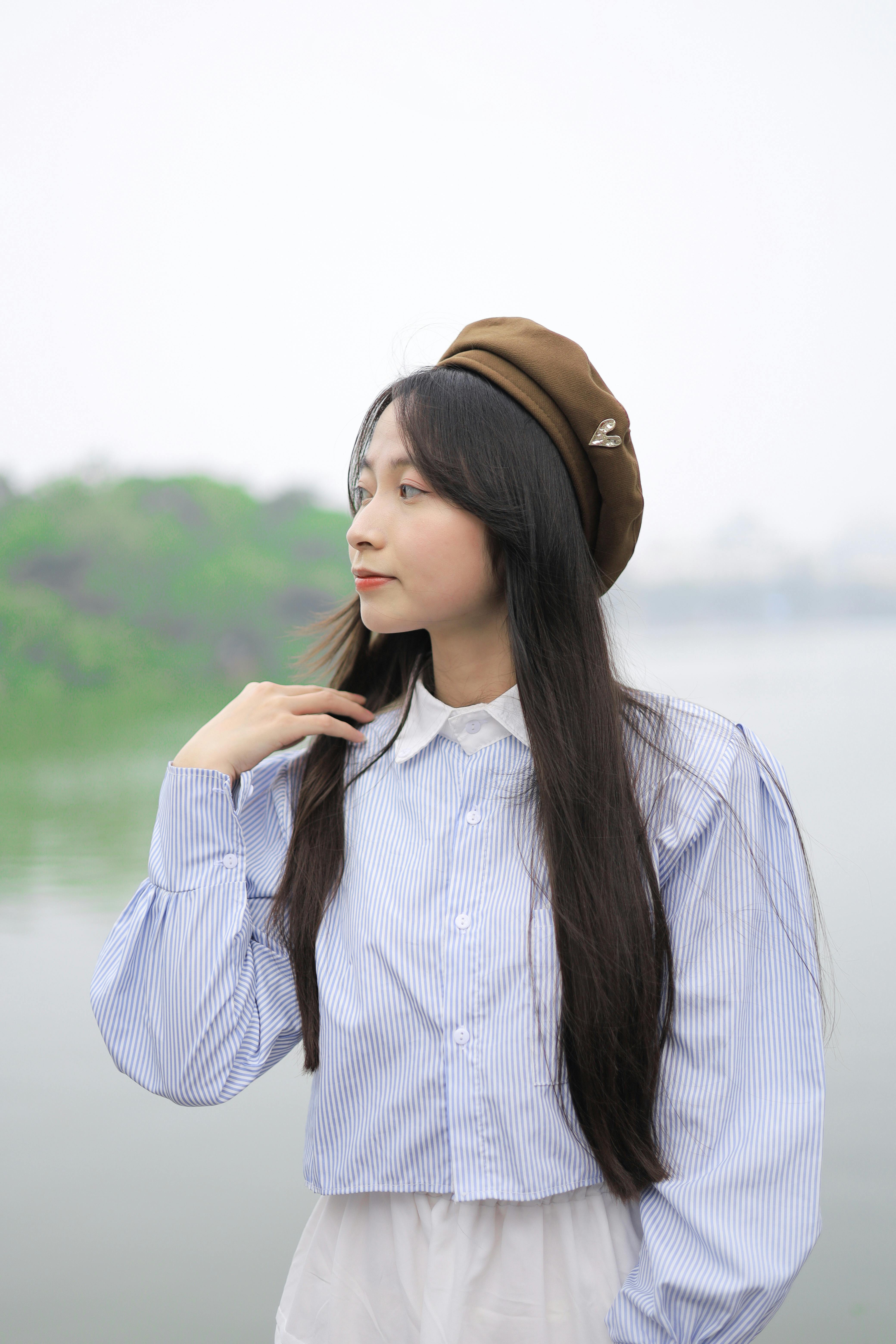 Elegant young woman wearing a beret by a serene lake in Hanoi, Vietnam.