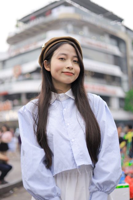 Portrait of a young woman with long hair in bustling Hanoi street, showcasing local fashion style.