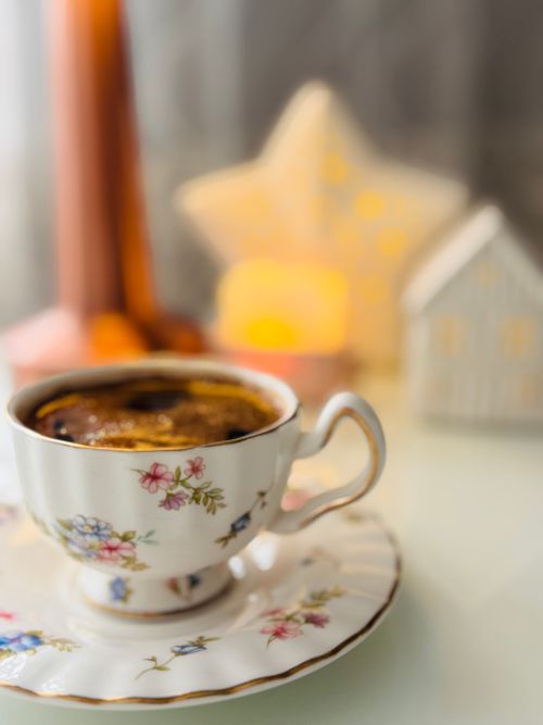 Free A floral teacup with coffee, lit by warm candlelight in a cozy setting. Stock Photo